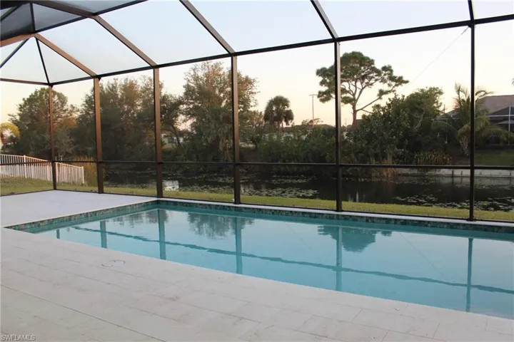 Pool at dusk featuring glass enclosure and a patio