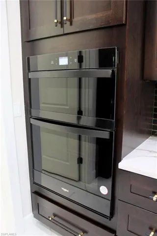 Room details featuring light stone countertops, dark brown cabinetry, and black double oven