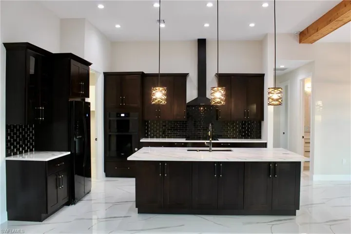 Kitchen with wall chimney range hood, double oven, decorative light fixtures, decorative backsplash, and a center island with sink