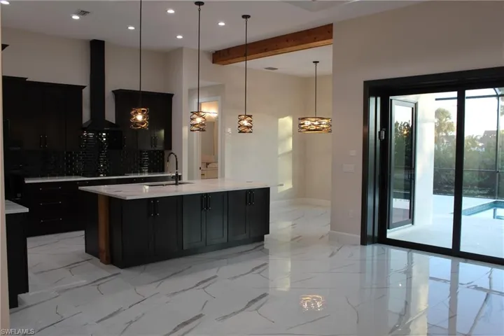 Kitchen featuring backsplash, wall chimney exhaust hood, sink, a center island with sink, and hanging light fixtures