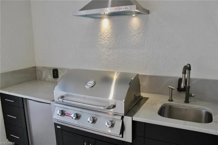 Kitchen featuring light stone countertops, sink, and wall chimney range hood