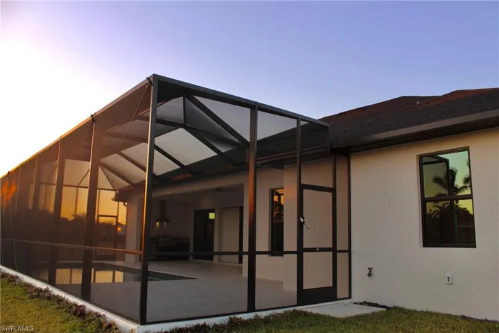Back house at dusk featuring ceiling fan, a lanai, and a patio