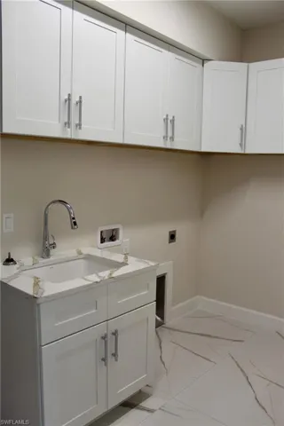 Laundry room with hookup for an electric dryer, hookup for a washing machine, cabinets, and sink