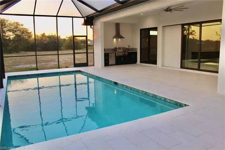 Pool at dusk featuring a patio, glass enclosure, ceiling fan, and exterior kitchen
