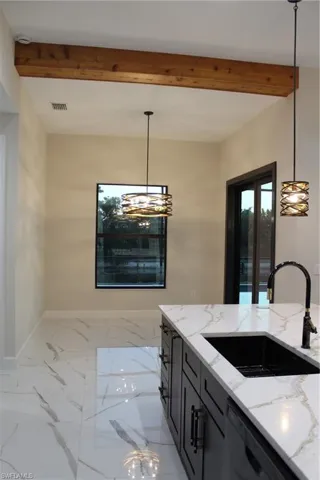 Kitchen featuring beam ceiling, light stone countertops, dishwasher, sink, and pendant lighting