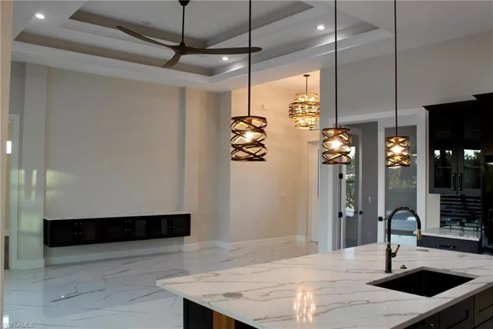 Kitchen featuring a raised ceiling, light stone counters, sink, and decorative light fixtures