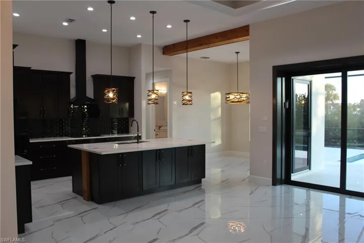 Kitchen featuring backsplash, sink, wall chimney range hood, decorative light fixtures, and an island with sink