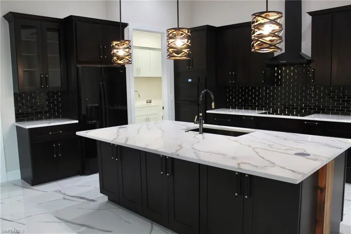 Kitchen with ventilation hood, sink, hanging light fixtures, and tasteful backsplash