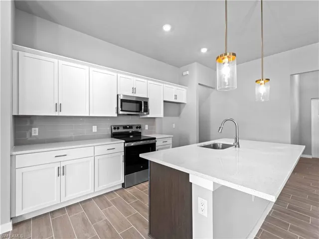 Kitchen featuring appliances with stainless steel finishes, wood tiled floors, white cabinets, decorative backsplash, and pendant lighting