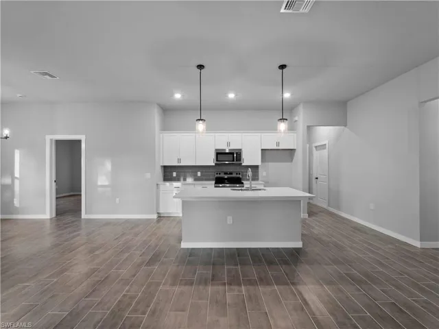 Kitchen featuring decorative backsplash, white cabinets, hanging light fixtures, appliances with stainless steel finishes, and a center island with sink