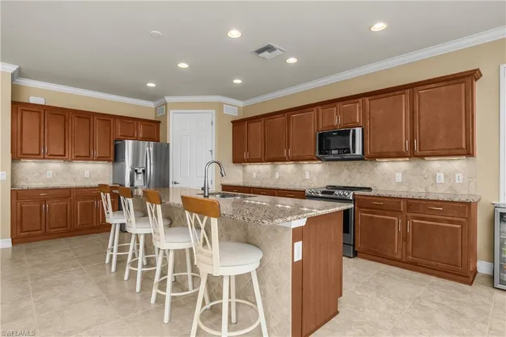 Kitchen featuring wood finish cabinetry, a breakfast bar, stainless steel appliances, ornamental molding, and recessed lighting