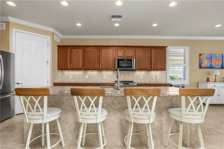 Kitchen featuring stainless steel appliances, wood finish cabinetry, light stone countertops, a kitchen breakfast bar, and a center island with sink