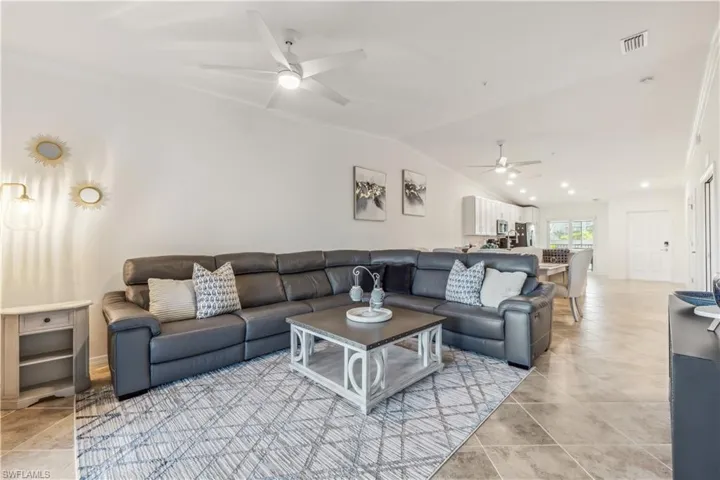 Living room featuring ceiling fan, vaulted ceiling, ornamental molding, and light tile floors
