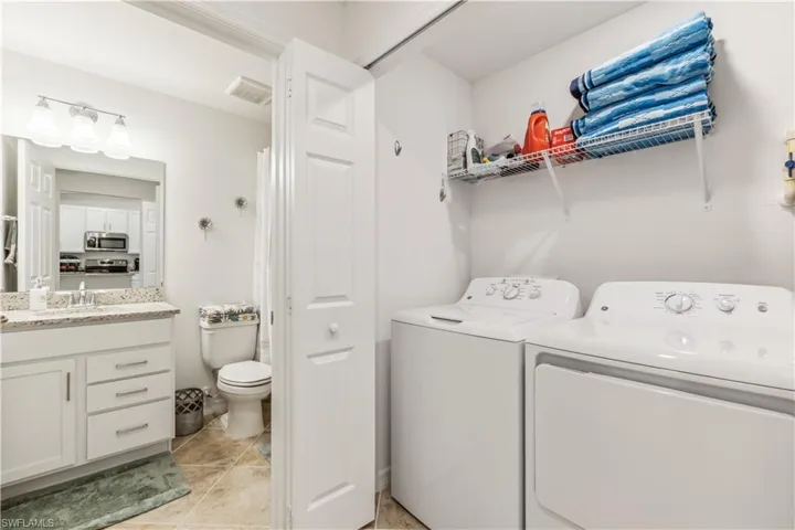 Clothes washing area with separate washer and dryer, sink, and light tile floors