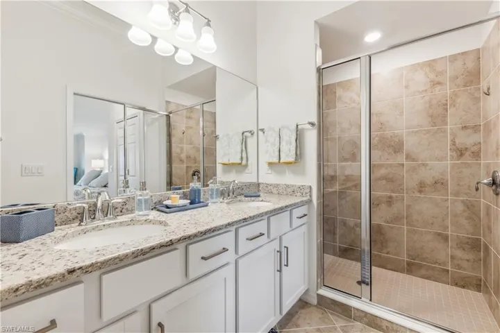 Bathroom with dual bowl vanity, tile flooring, an enclosed shower, and a chandelier
