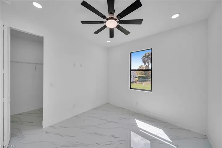 Unfurnished bedroom featuring a walk in closet, a ceiling fan, recessed lighting, and light marble finish flooring