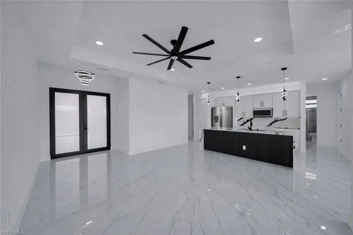 Unfurnished living room featuring a ceiling fan, french doors, recessed lighting, light marble finish floors, and a tray ceiling