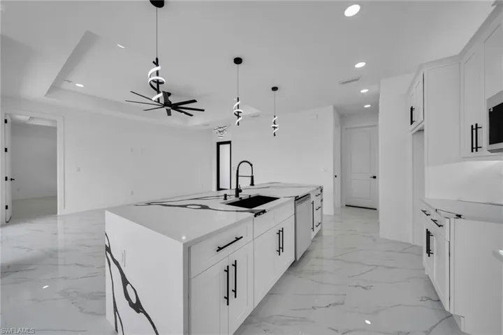 Kitchen with a kitchen island with sink, light stone counters, pendant lighting, white cabinetry, and a ceiling fan