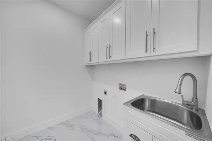 Laundry room with hookup for an electric dryer, light marble finish floors, hookup for a washing machine, and cabinet space