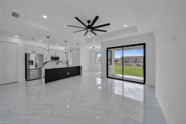 Unfurnished living room with a tray ceiling, light marble finish flooring, and ceiling fan