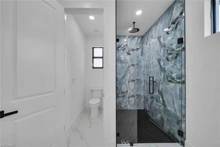 Bathroom with a marble finish shower, light marble finish floors, and recessed lighting