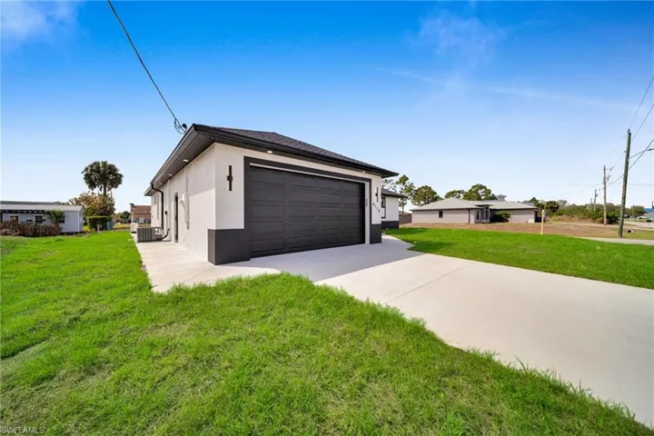 View of property exterior featuring a yard, a garage, stucco siding, and driveway
