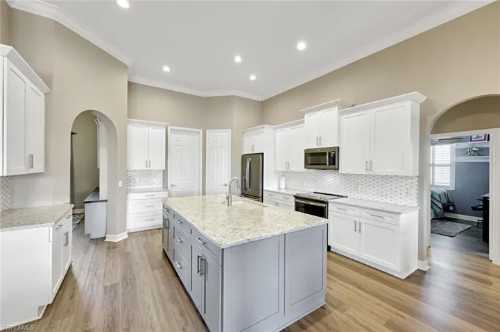 Kitchen featuring arched walkways, white cabinetry, crown molding, and recessed lighting