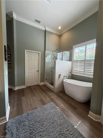 Bathroom featuring a stall shower, a soaking tub, dark wood-style flooring, ornamental molding, and recessed lighting