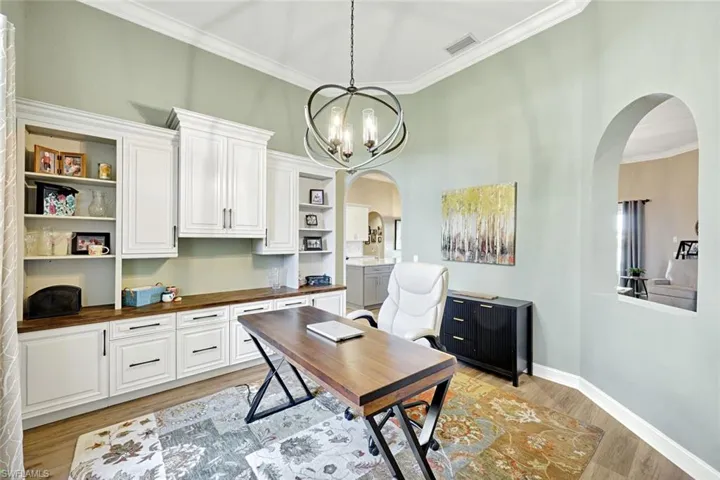 Office area featuring crown molding, light wood-style floors, arched walkways, and a chandelier