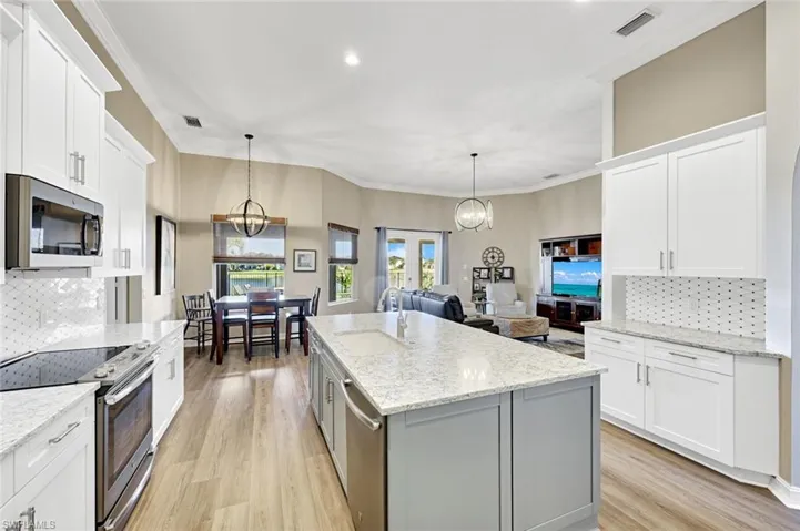 Kitchen with backsplash, appliances with stainless steel finishes, ornamental molding, white cabinets, and pendant lighting