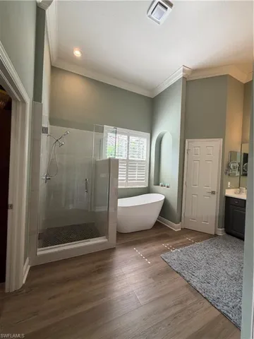 Bathroom with a stall shower, vanity, a freestanding tub, dark wood-style flooring, and ornamental molding