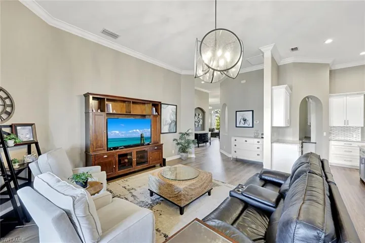 Living area featuring arched walkways, ornamental molding, wood finished floors, and a chandelier