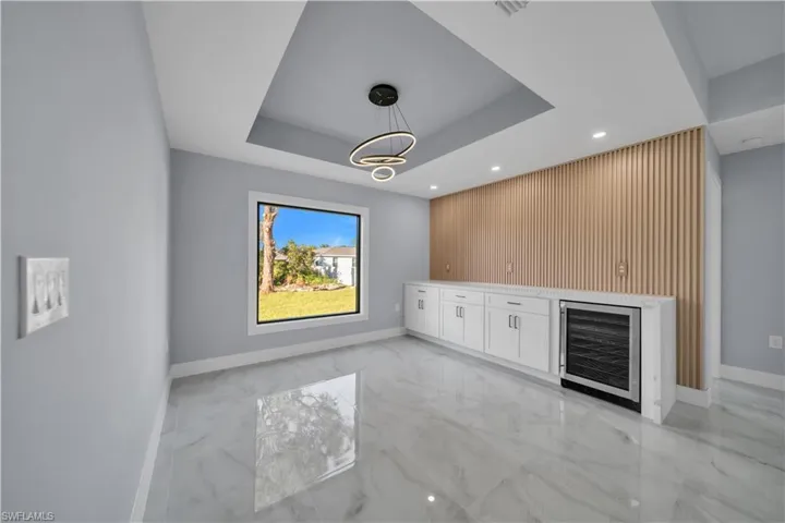 Bar area with white cabinets, decorative light fixtures, a raised ceiling, light marble finish flooring, and recessed lighting