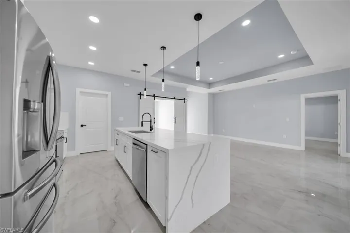 Kitchen featuring stainless steel appliances, light stone counters, white cabinetry, pendant lighting, and a raised ceiling