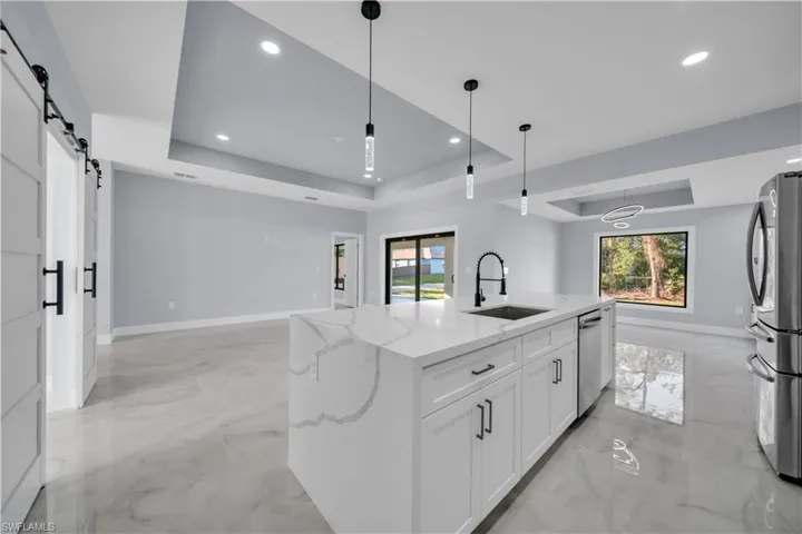 Kitchen featuring a tray ceiling, a barn door, light marble finish flooring, light stone countertops, and white cabinetry