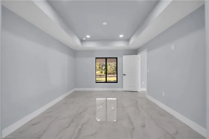 Empty room featuring light marble finish floors, recessed lighting, and a raised ceiling