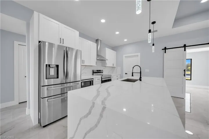 Kitchen featuring appliances with stainless steel finishes, a barn door, white cabinetry, recessed lighting, and light marble finish floors