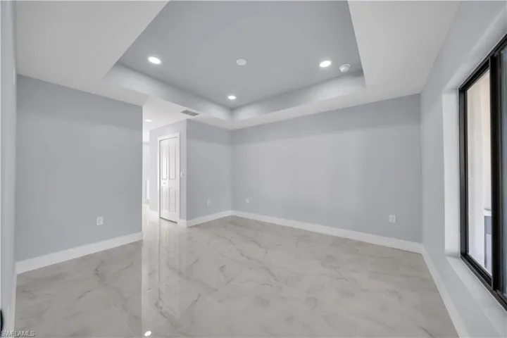 Empty room with a raised ceiling, recessed lighting, and light marble finish floors