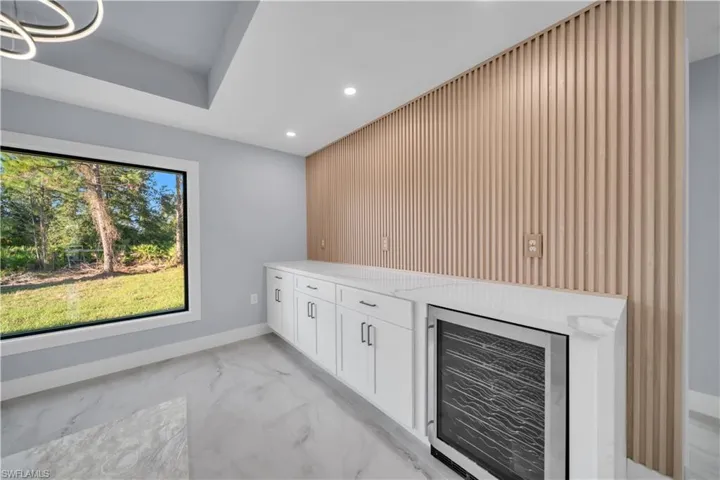 Bar area with beverage cooler, white cabinets, light stone countertops, recessed lighting, and light marble finish flooring