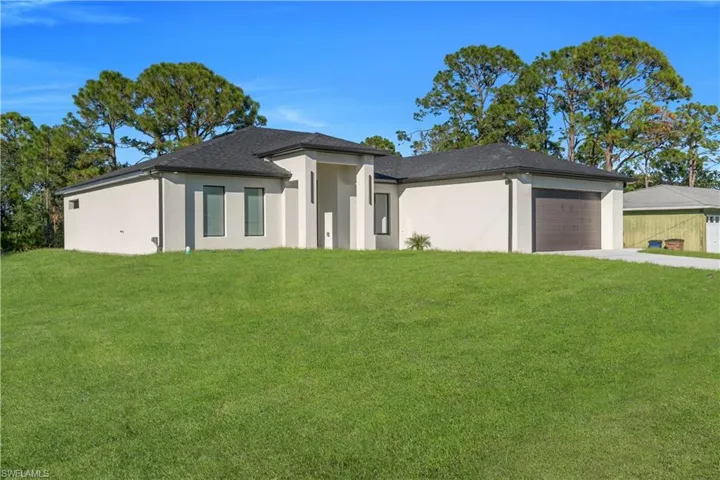 Prairie-style home with a front yard, an attached garage, driveway, and stucco siding