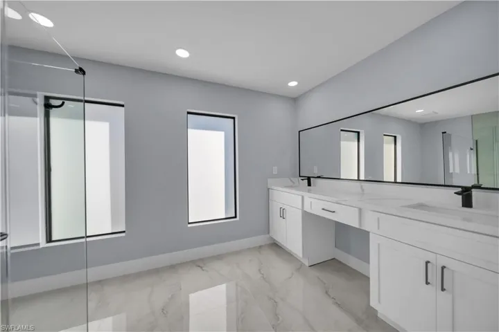 Full bathroom featuring a shower stall, light marble finish floors, recessed lighting, and double vanity