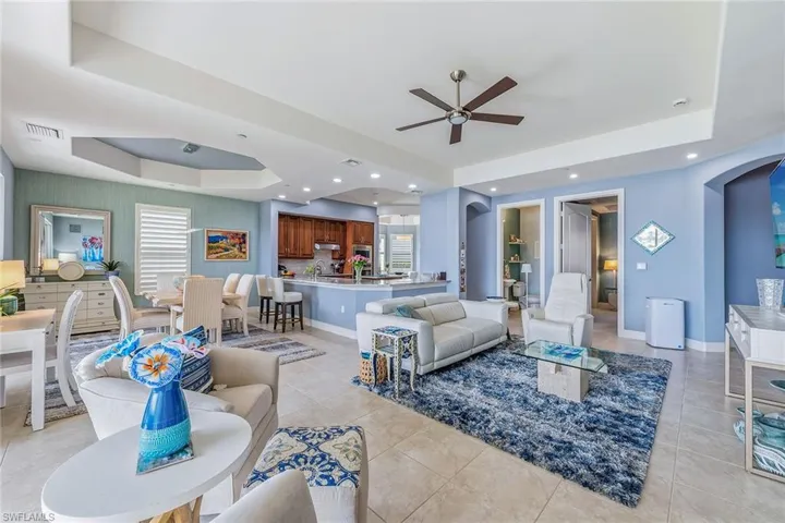 Living room with a raised ceiling, arched walkways, ceiling fan, light tile patterned flooring, and recessed lighting