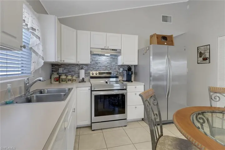 Kitchen featuring stainless steel appliances, lofted ceiling, sink, white cabinetry, and light tile patterned flooring