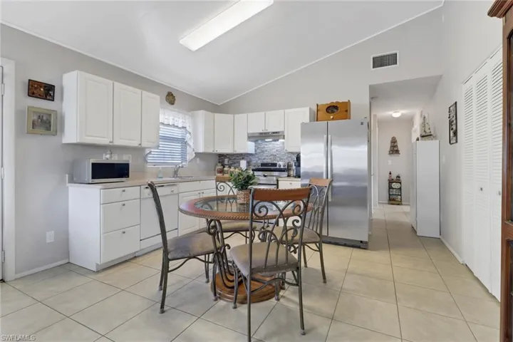 Kitchen featuring vaulted ceiling, appliances with stainless steel finishes, light tile patterned floors, white cabinetry, and backsplash