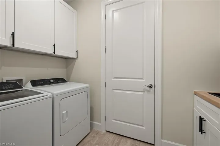 Laundry room with light wood-look tile floors, cabinets, and independent washer and dryer