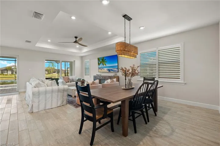 Dining area with ceiling fan, a raised ceiling, ornamental molding, and light wood-look tile flooring