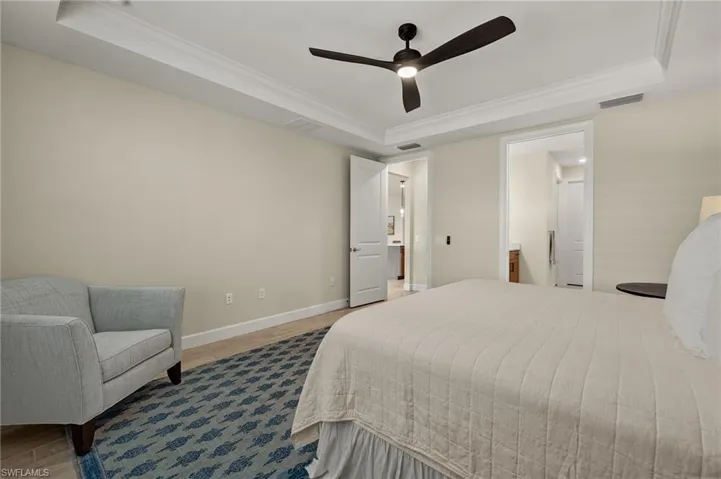 Bedroom featuring wood-look tile flooring, a tray ceiling, ceiling fan, and ornamental molding