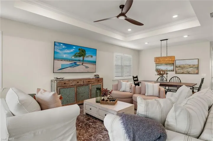 Living room with a raised ceiling, ceiling fan, and crown molding