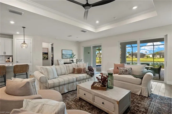 Living room with a raised ceiling, crown molding, light wood-look tile flooring, and ceiling fan