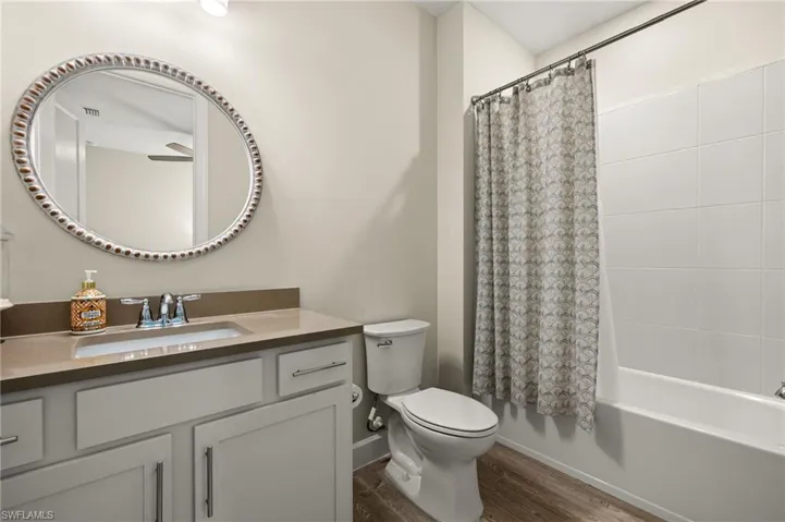 Full guest bathroom featuring shower / bath combination with curtain, vanity, wood-look tile flooring, and toilet